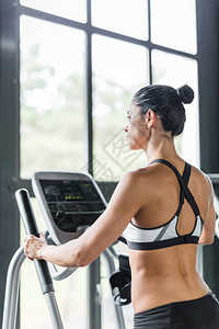 在现代健身房与大窗对面运动时使用椭圆机锻炼的美丽运动女图片
