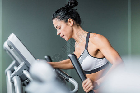 在现代健身房密集锻炼期间使用椭圆机进行运动的体身健壮妇图片