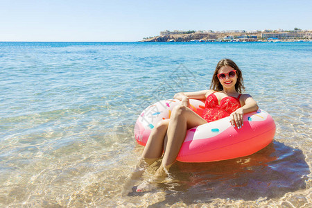 美丽的年轻妇女放松在充气甜甜圈在海高清图片