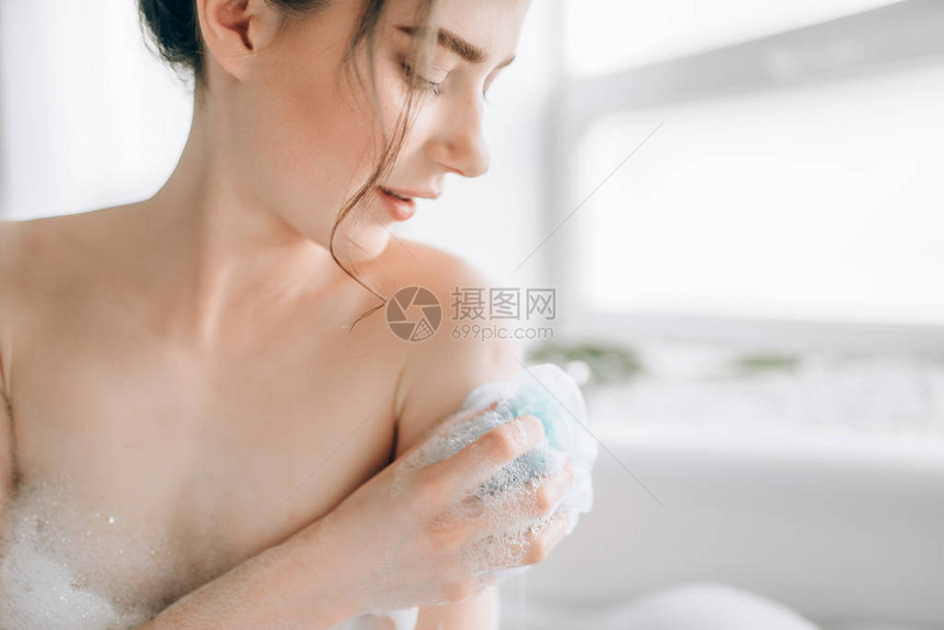 使用海绵在浴缸中的年轻妇女泡沫放松和水疗图片