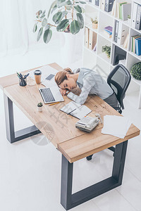 过度劳累的成年女商人睡在工作场所的视角图片