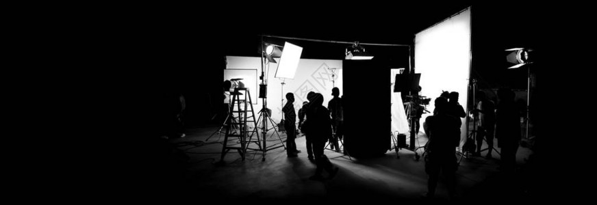 电影摄制组灯光师和摄像师与导演一起在大工作室工作配备专业设备背景图片