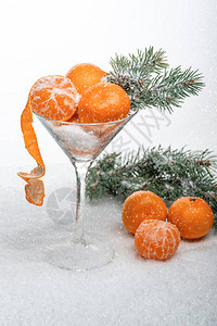 雪地里放着一杯加了橘子的马提尼酒玻璃下面还有三个橘子和一根圣诞树枝下雪了背景图片