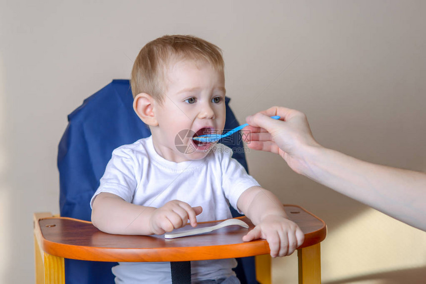 小男孩坐在厨房的椅子上张开嘴吃东西手里拿着一勺粥喂饭图片