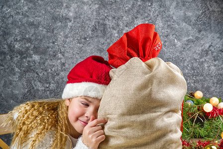 小金发女孩戴着小黑帽的红帽子躲在圣诞老人包后面图片