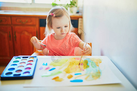 可爱的小女孩在家里幼儿园或学前班用五颜六色的水彩画作背景图片