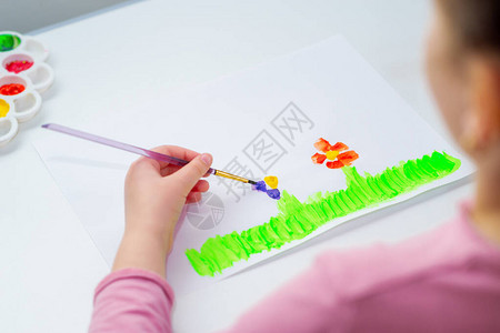孩子的手在绿草上用水彩笔在白纸上画花图片