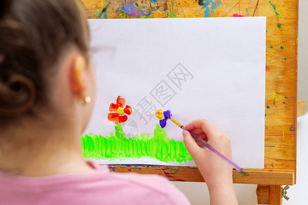 小女孩的手在绿草上画花用水彩刷在图片