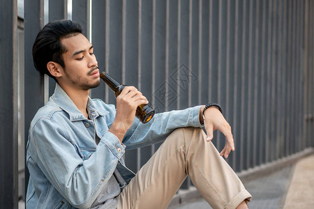 失业的亚洲年轻人带着啤酒瓶独自坐在路边图片