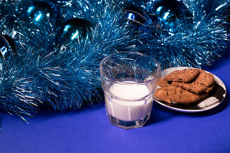 新年玩具和蓝底装饰品旁边的圣诞老人牛奶饼干和饼干图片