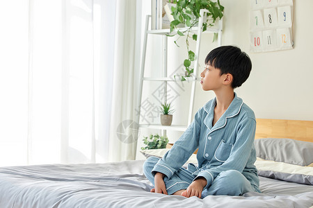 早晨穿睡衣坐在床上的小男孩背景图片