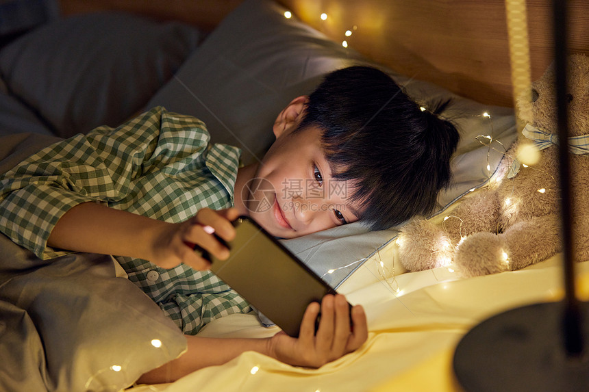 躺在床上玩手机的男孩图片
