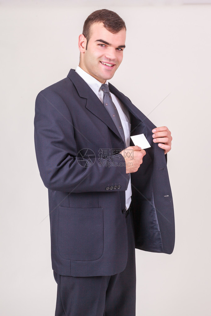 时尚英俊的年轻商人在摄影机前微笑从他的夹克口袋里拿一张名片白图片