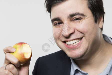 黑头发的欧洲商人带着笑脸从一个小苹果里咬了一口他的眼睛睁着背景图片