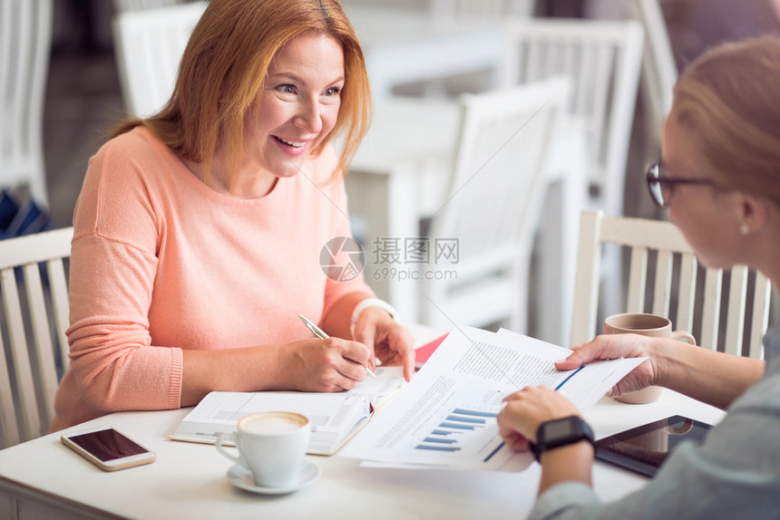 愉快的谈话快乐的年长妇女坐在桌边做笔记和进行访谈图片