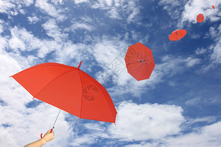 红伞手握着蓝天空和云底背景的红色雨伞图片