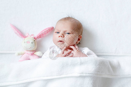 可爱的新生婴儿玩粉红色毛绒动物拨浪鼓玩具在家里的白色床上新出生的孩子图片