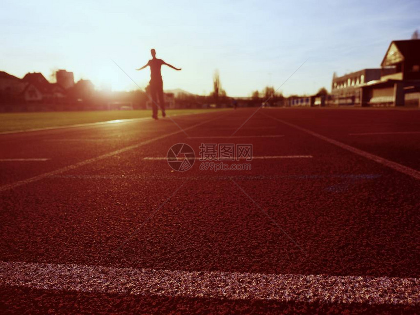 高个子在体育场的红色跑道上奔跑在令人惊叹的日落时穿着训练服的运动员体育和健康生活方式概念和慢跑图片