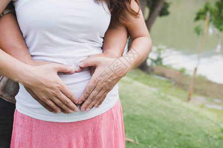 年轻的亚洲妇女和她的丈夫一起抚摸着她怀孕的腹部图片