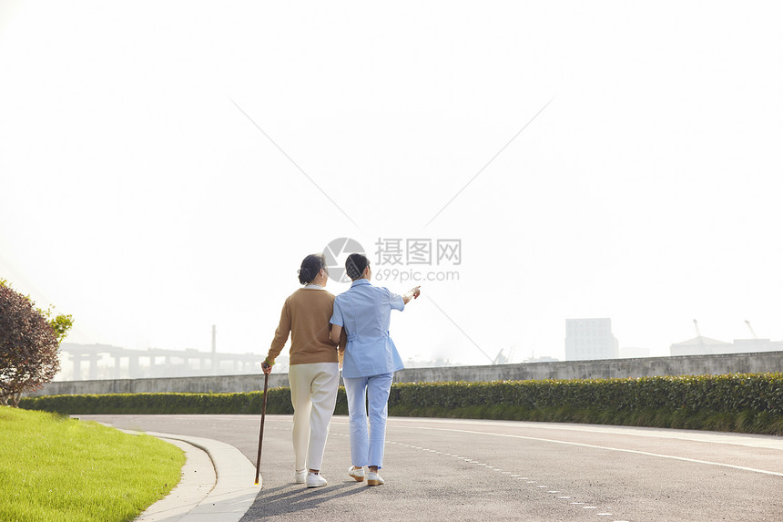 女护工陪伴老人公园散步背影图片