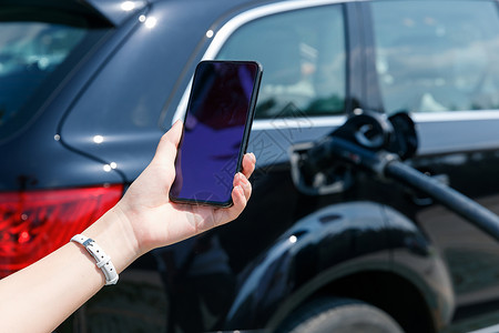 青年女人使用手机自助充电汽车背景图片