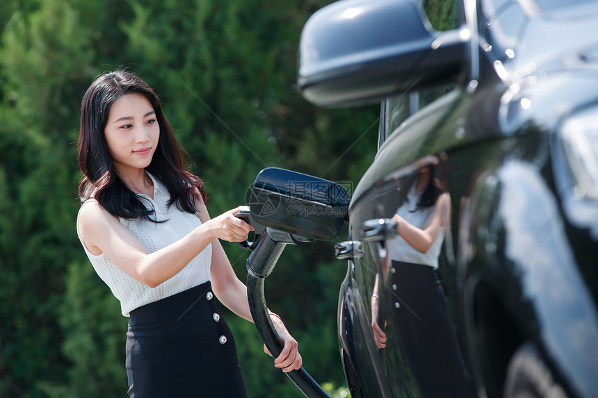 青年女人拿着充电准备给汽车充电图片