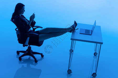 商务女士坐在办公桌前看手机高清图片