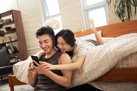 青年情侣趴在床上玩手机背景图片