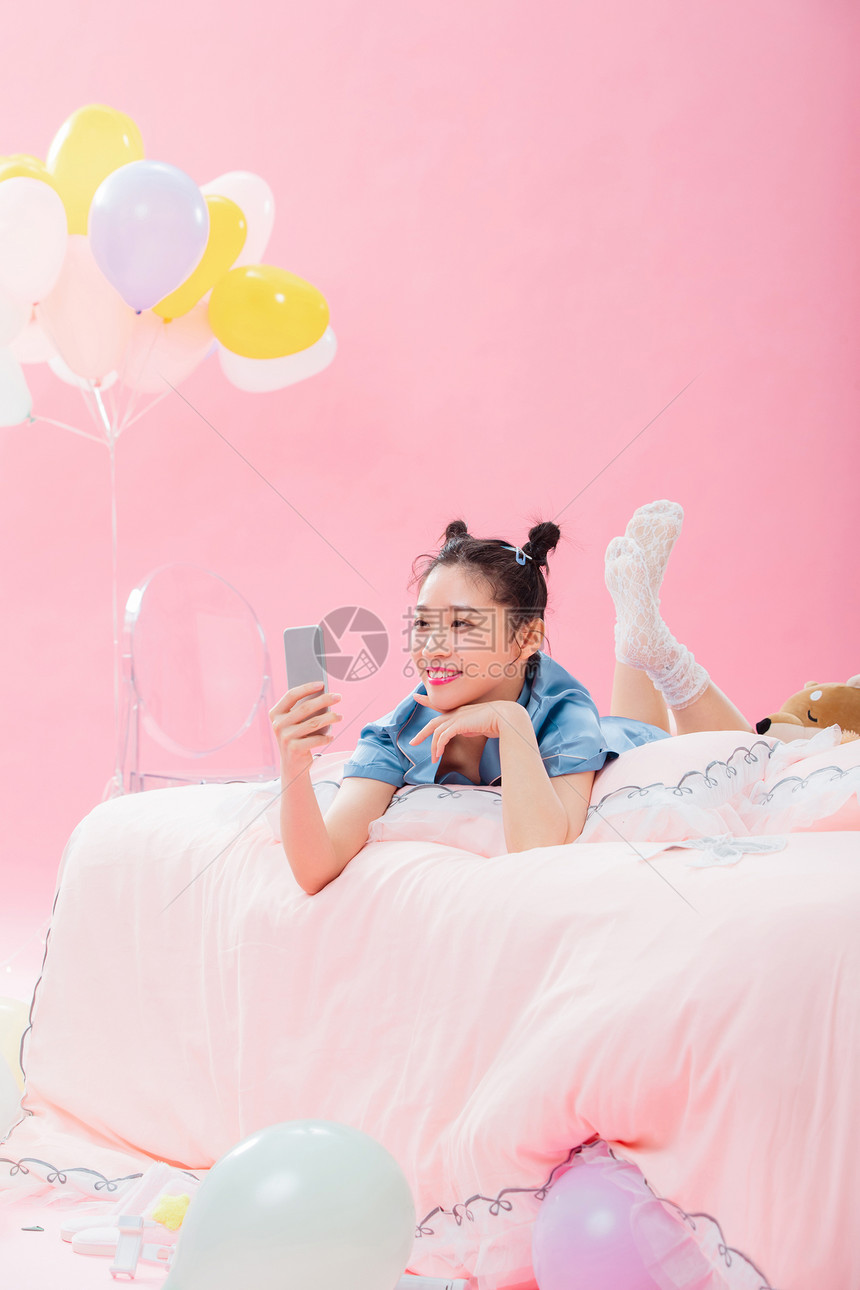 年轻女孩趴着在床上使用手机图片