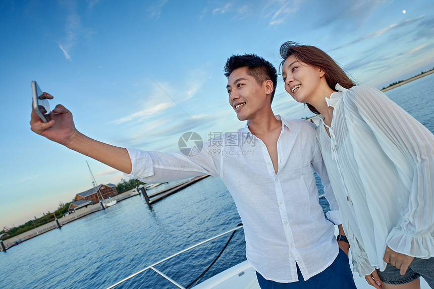 青年夫妇站在游艇上用手机拍照图片