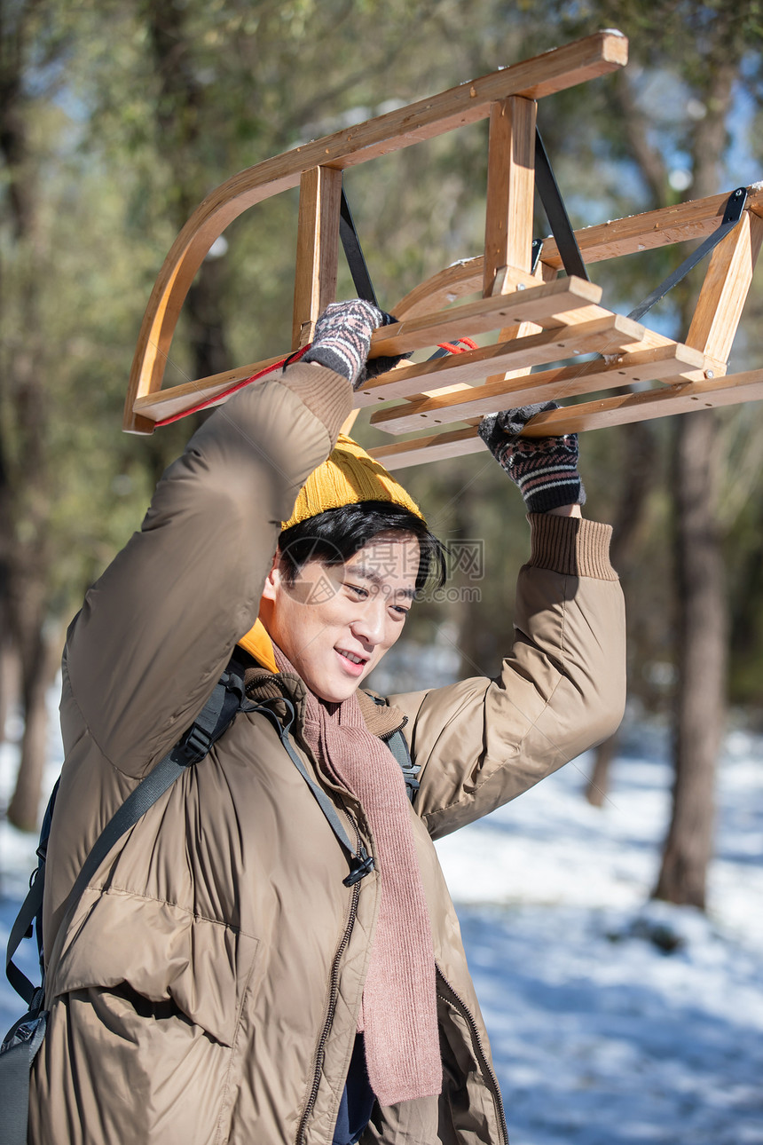 雪地上步行举着雪橇的青年男人图片