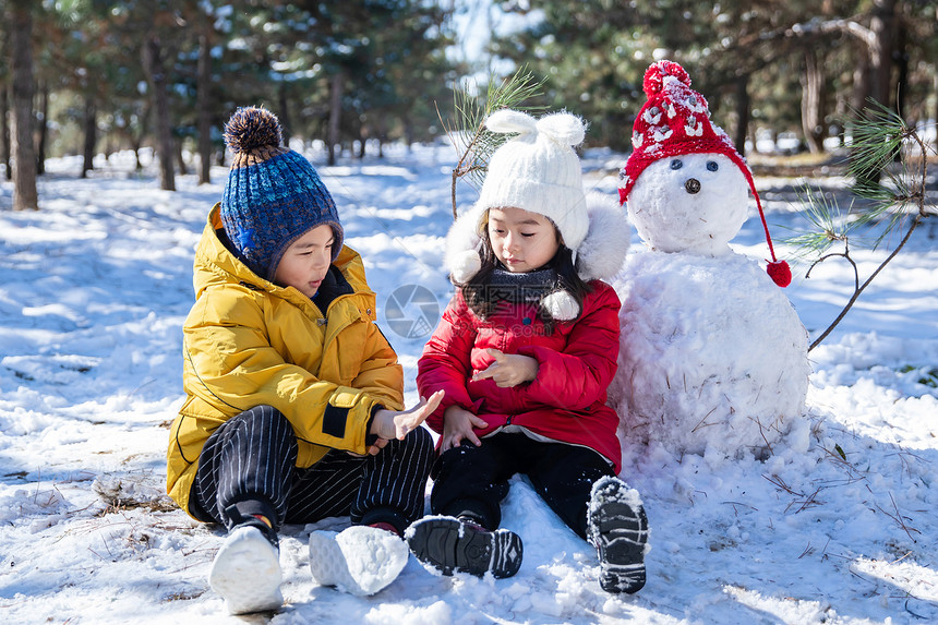 坐在雪地上玩耍的儿童和雪人图片