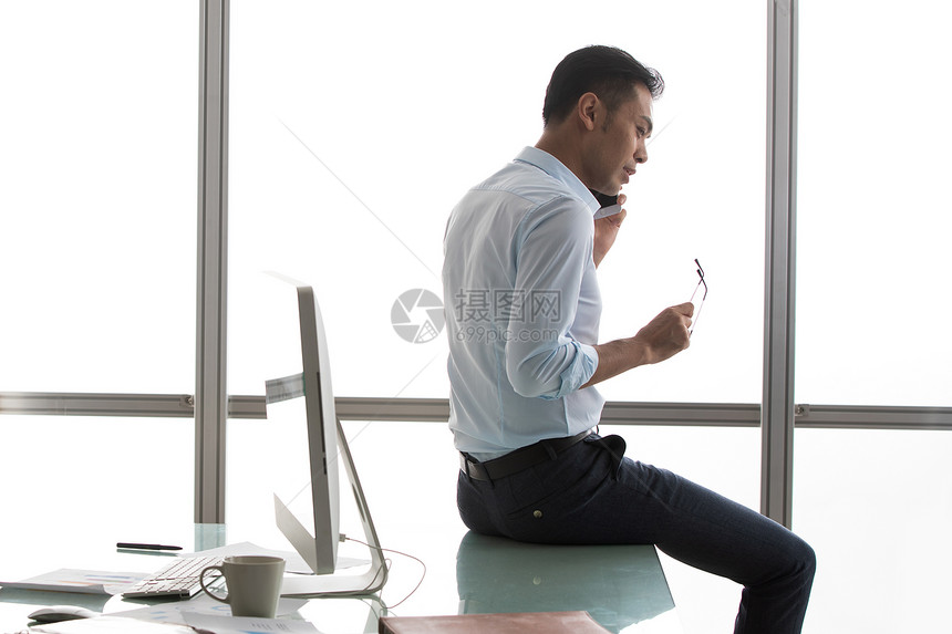 坐在办公桌上打电话的商务男士图片