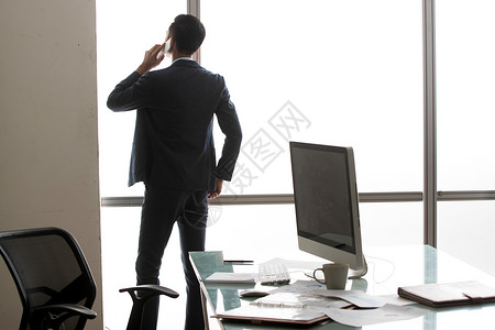 商务男士在窗户前打电话的背影背景图片
