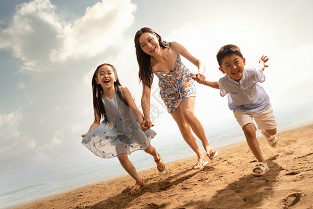 沙滩上母女年轻母亲牵着两个孩子在沙滩上奔跑背景