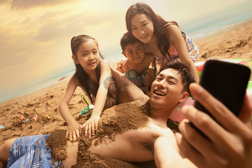 沙滩上男人拿手机和妻子孩子自拍图片