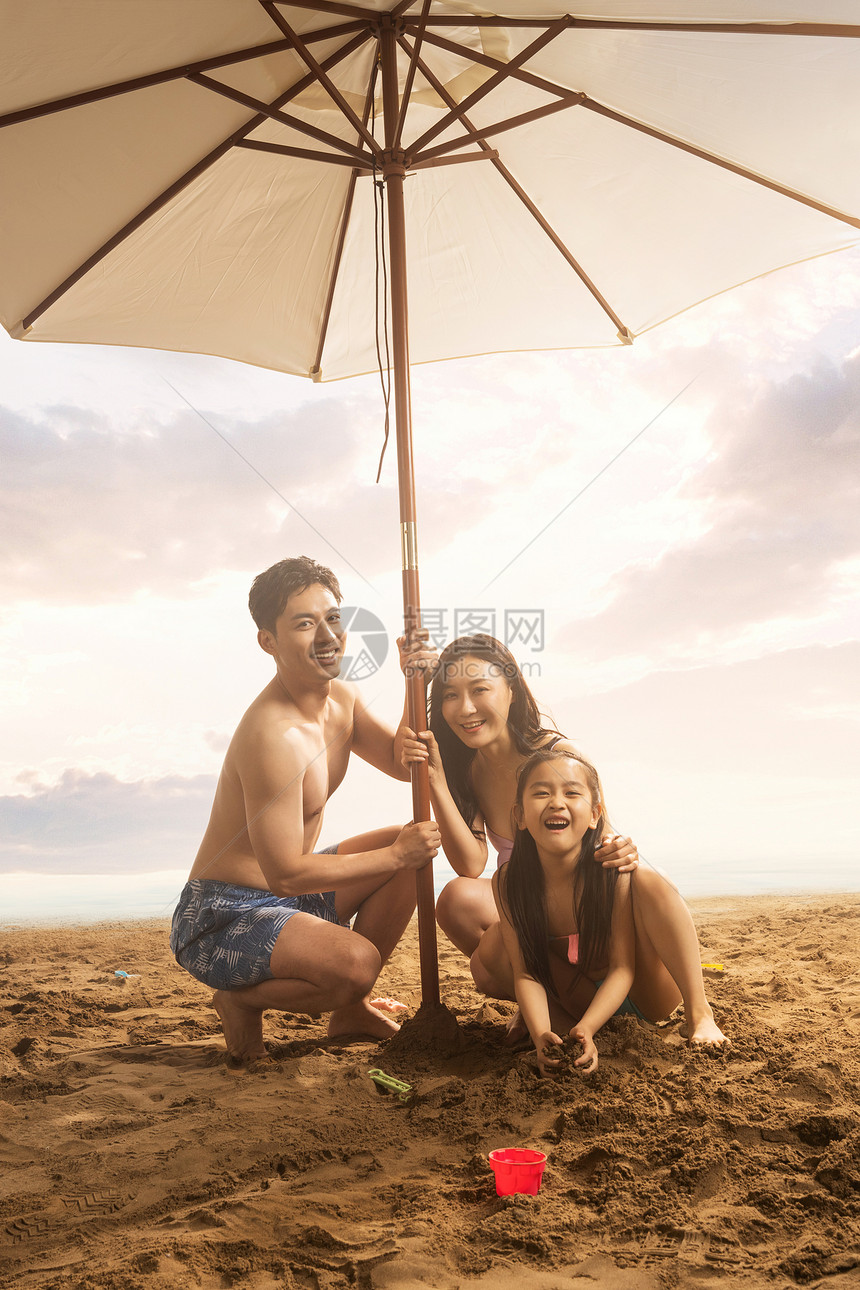 海滩上遮阳伞下的三口之家图片