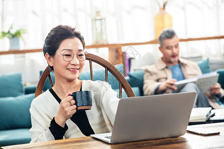 端着杯子的女士中老年女士在家端着杯子使用电脑背景