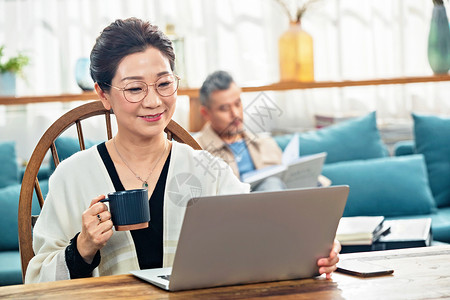 专注于前景中老年女士在家端着杯子使用电脑背景