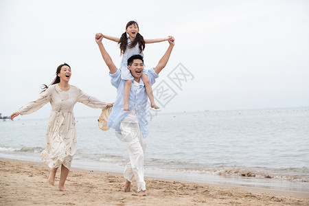 跳起来的女孩幸福的一家三口在海边玩耍背景