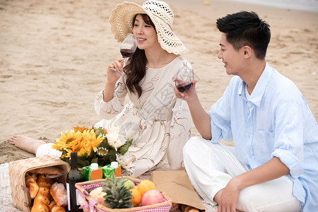 浪漫的青年夫妇坐在沙滩上喝红酒高清图片