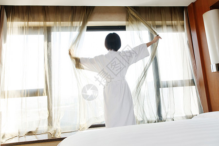 床帘年轻女人在酒店房间里拉开窗帘背景