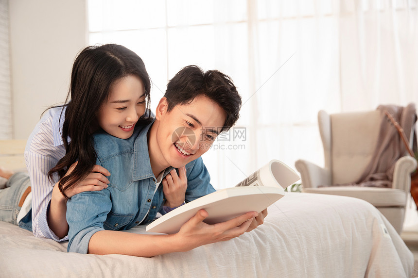 亲密的年轻情侣趴在床上看书图片