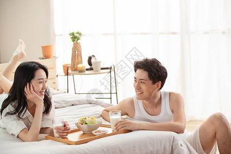 快乐的年轻情侣在床上吃早餐高清图片