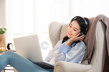 青年女性使用电脑听音乐快乐的女青年坐在沙发上使用笔记本电脑背景