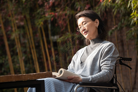 户外老年女人坐在轮椅上看书高清图片