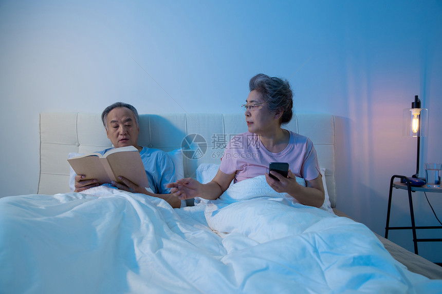 老年夫妇坐在床上看书看手机图片