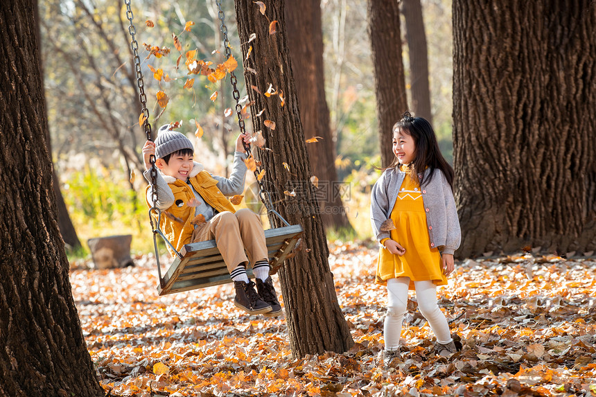 快乐的女孩往荡秋千上的男孩身上抛树叶图片