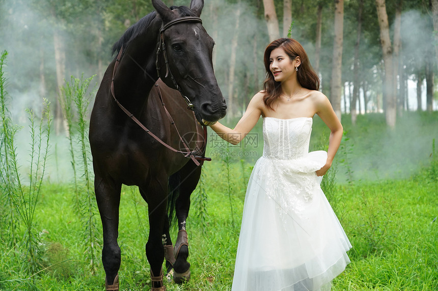 树林里漂亮的年轻女人牵着马图片