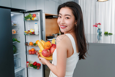 拿着水果的青年女人站在冰箱前轻松高清图片素材